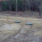 A completed gravity septic system on a new home. Notice the 2x4 behind the septic tank. We mark our D boxes like this so that everyone knows where it is easily during the construction phase. The board can be removed later, but we suggest just cutting it down to the grass line.